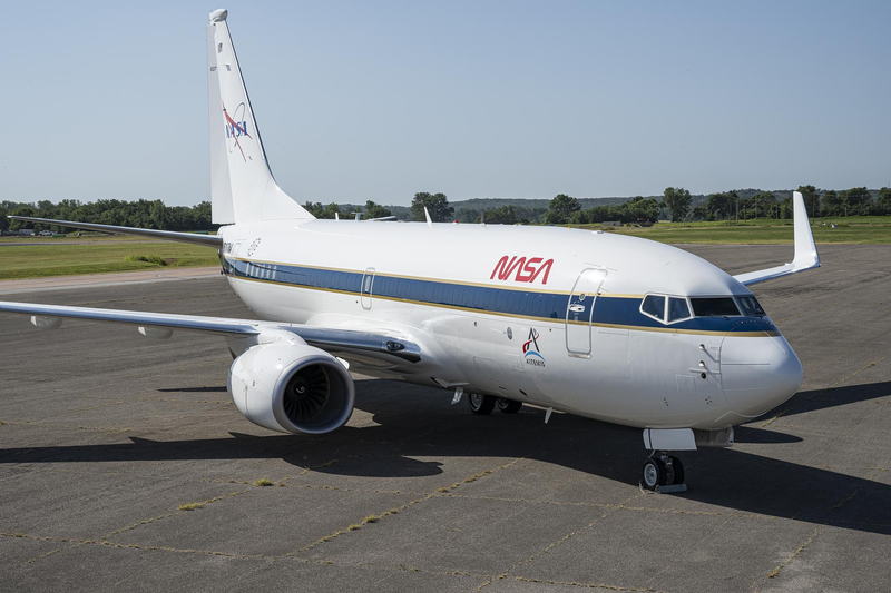 A white NASA Boeing 737 with a blue cheatline sits on an airport apron under a clear sky.