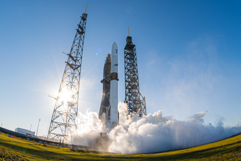 A New Glenn booster rises past its lightning towers at Cape Canaveral in November 2025, venting cryogenic hydrogen as the first stage lights seven engines.