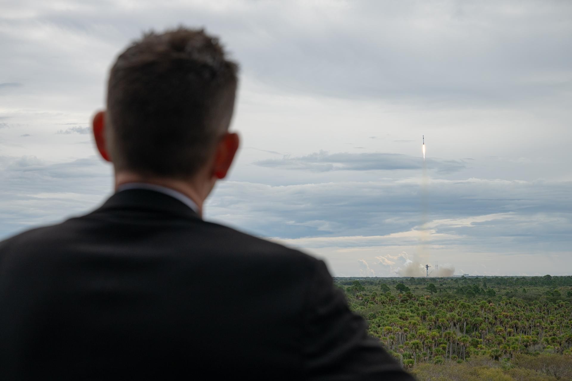 A NASA official watches as a SpaceX Falcon 9 climbs into cloudy skies over Cape Canaveral on October 1, 2026, carrying the four Crew-13 astronauts toward the International Space Station.