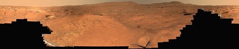 A 360-degree Mastcam-Z panorama of Turquoise Bay in the Margin Unit along the inner edge of Jezero Crater, stitched from 818 natural-color images Perseverance captured between October 5 and 16, 2023, sols 933 through 944 of the mission. The rolling brownish-red Martian terrain stretches to the horizon, with the rover itself visible as a small bright glint near the center of the panorama.